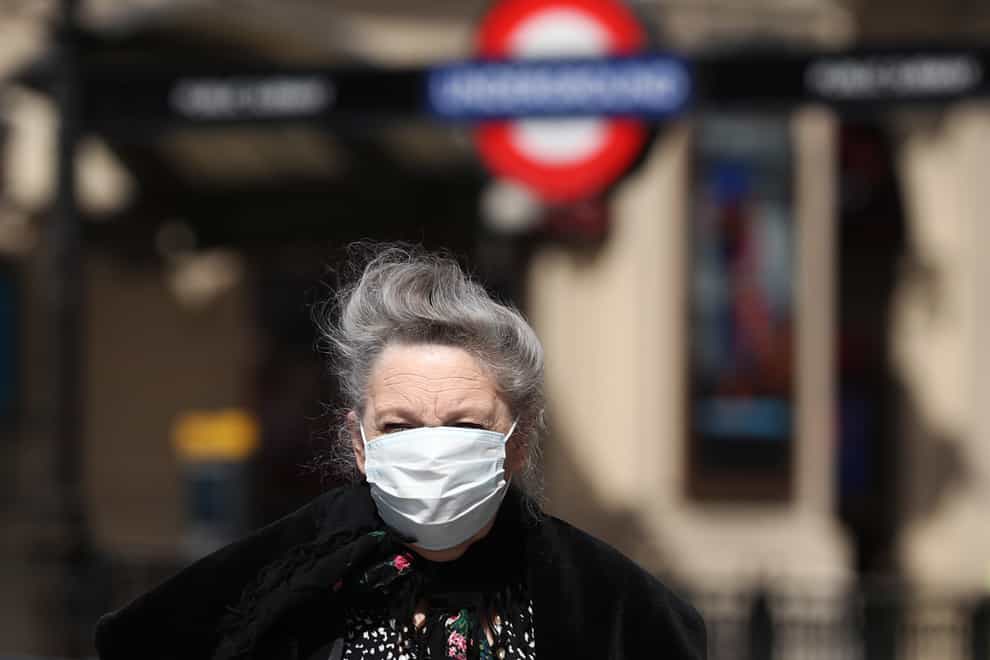 A woman with a face mask walking past Piccadilly Circus London Underground station