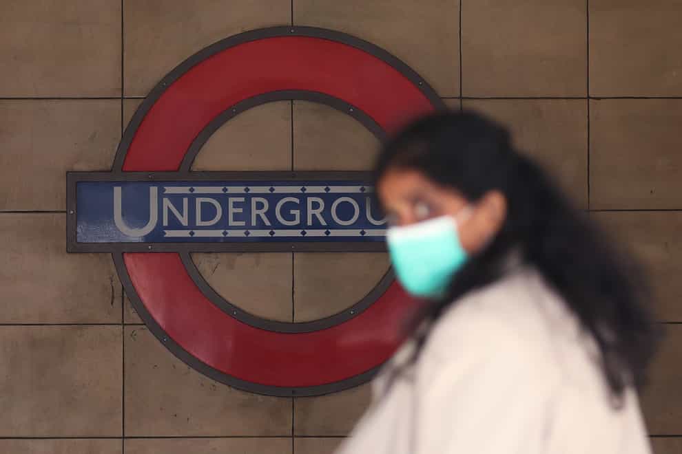 A woman wearing a facemask in front of a London Underground sign