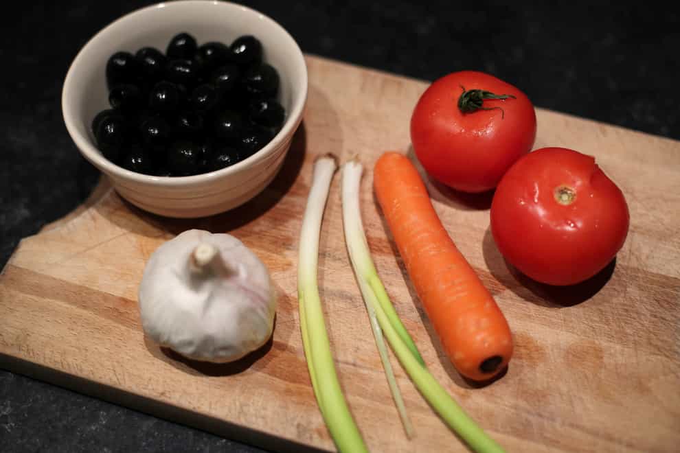 A bowl of black olives, tomatoes, spring onion, a carrot and a garlic bulb on a chopping board