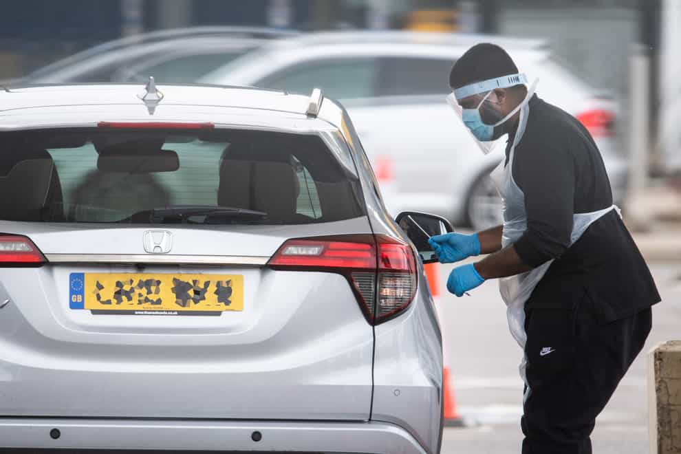 A tester wearing PPE holds a swab at a drive-through site