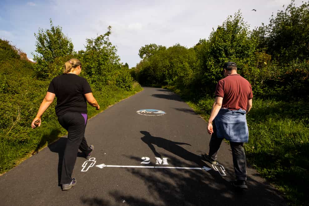 People walk past a 2m social distancing sign on the Comber Greenway in east Belfast
