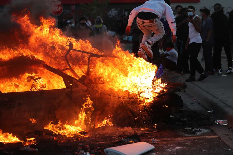 A man jumps off a burning car among demonstrators in the streets in Minneapolis during a third night of protests following the death of George Floyd 