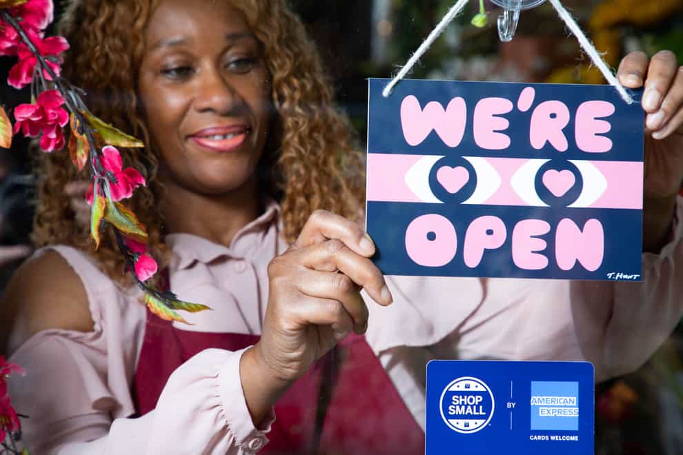 A woman hangs a 'We're Open' sign on a shop door