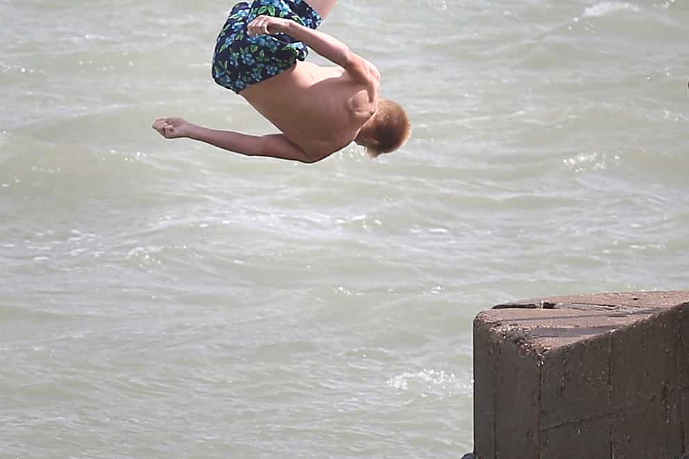 A boy jumps into the sea from a jetty on Dover sea front.