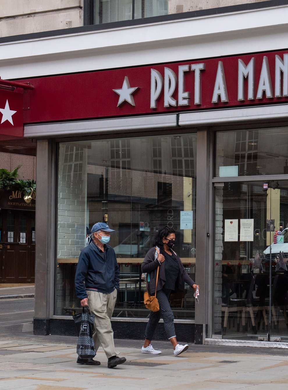 People wearing protective face masks walk past a closed Pret a Manger shop