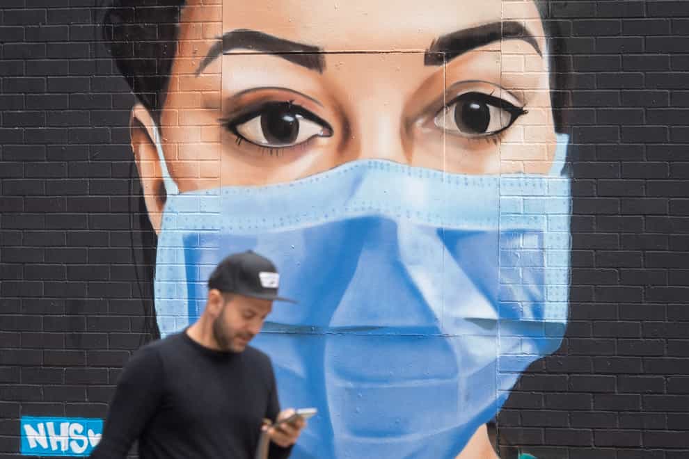 A man walks past a mural of a nurse wearing a face mask