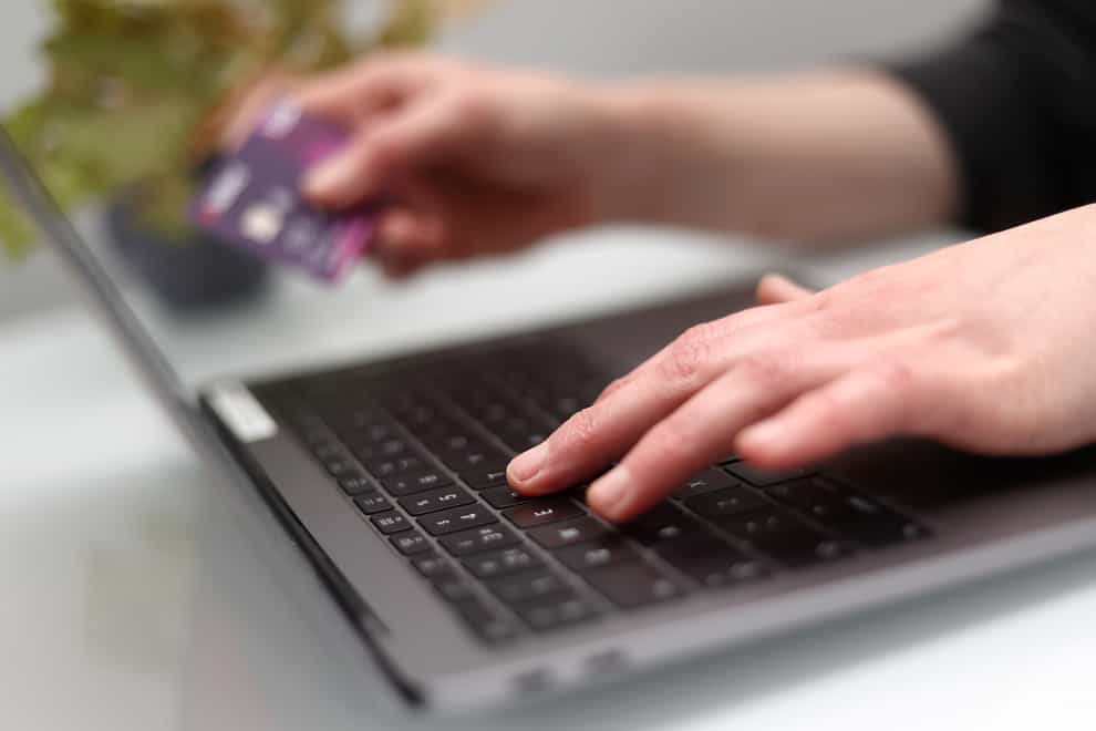 A woman holding a bank card uses a laptop