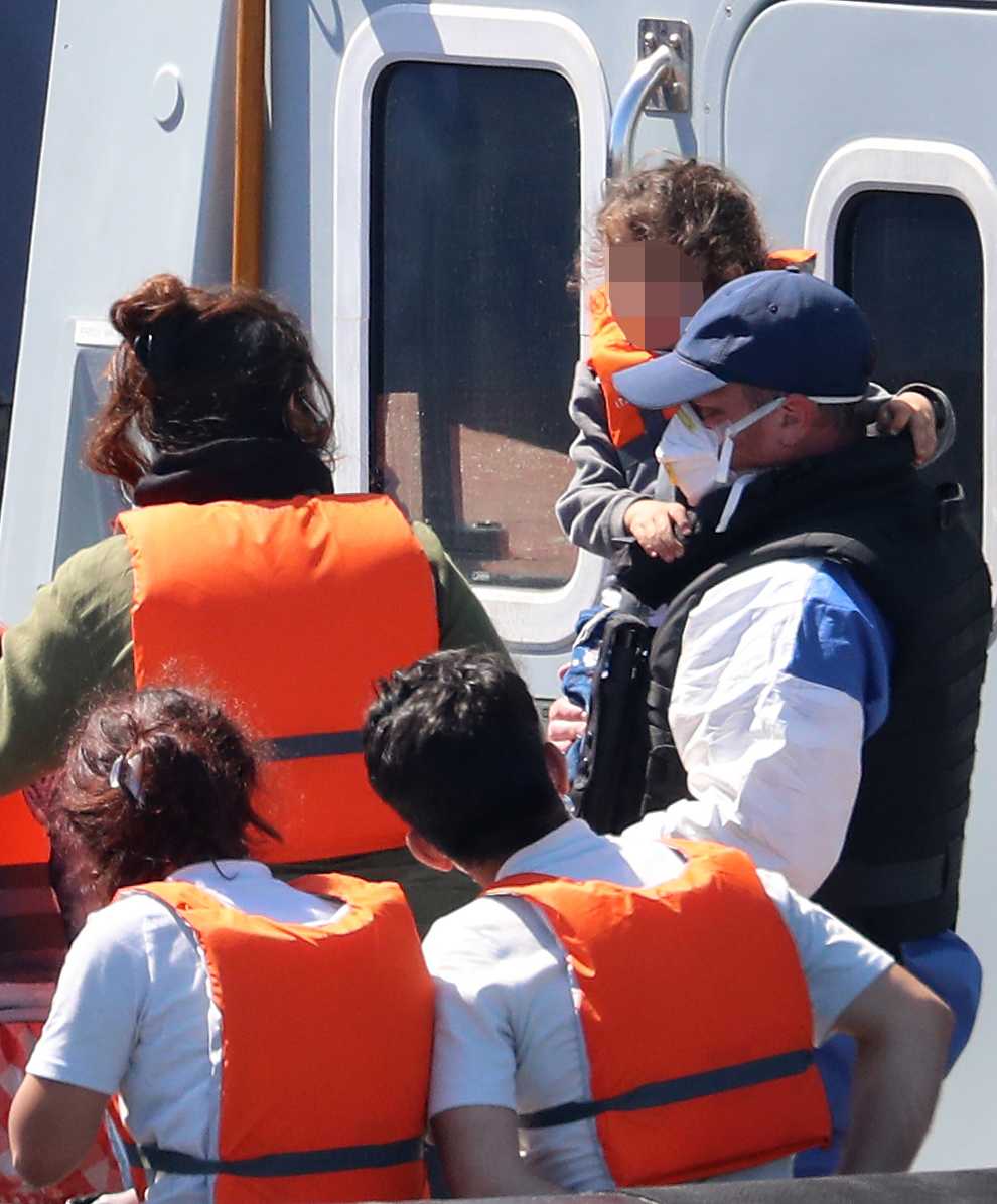 A Border Force officer escorts a young family thought to be migrants from a Border Force vessel