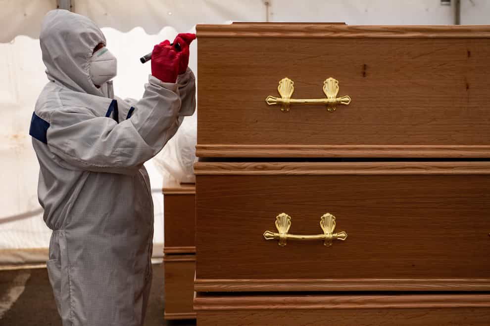 A funeral worker wearing PPE checks coffins