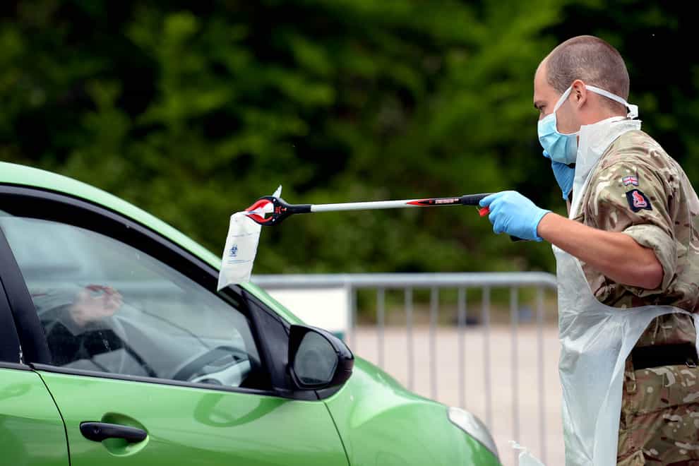 A person passes a completed coronavirus self-test package through a car window
