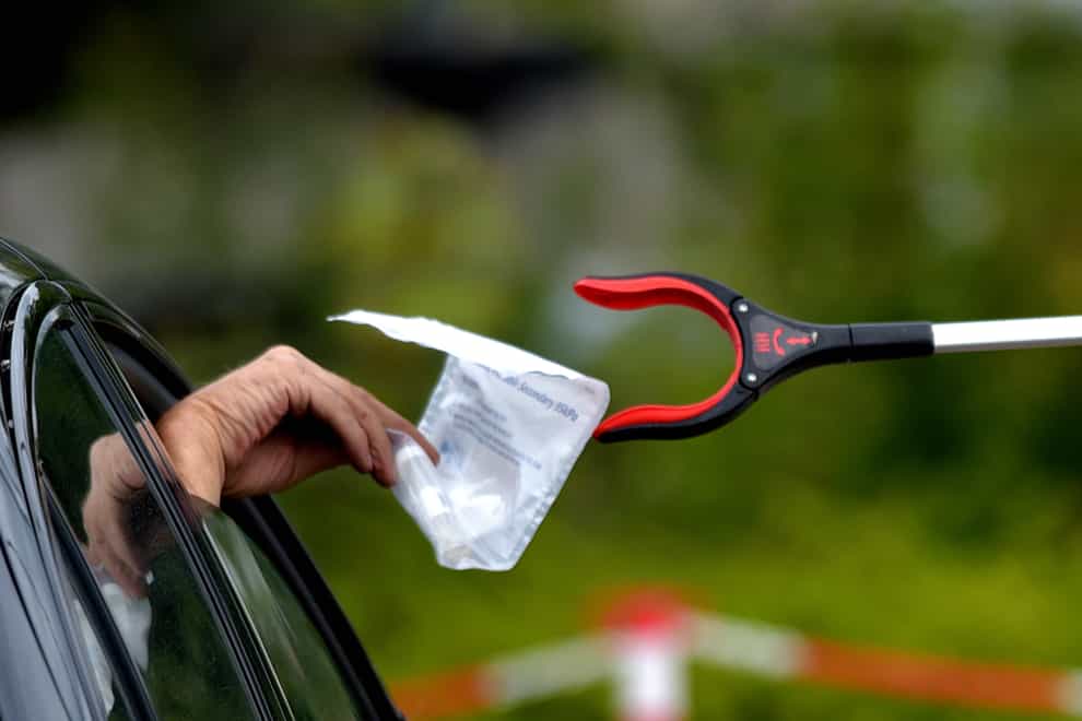 A person passes a completed coronavirus self test package through a car window (Nick Ansell/PA)