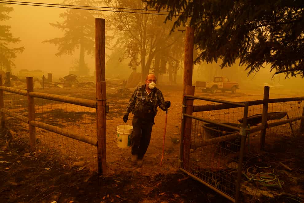 George Coble carries a bucket of water to put out a tree still smouldering on his property destroyed by a wildfire
