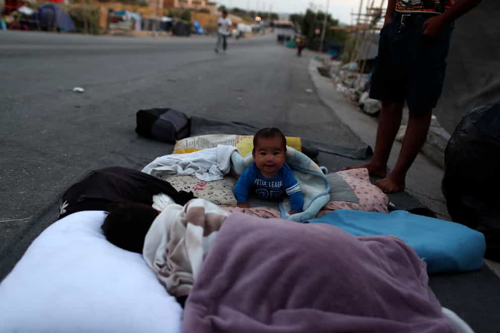 A baby crawls as migrants remain camped out on a roa
