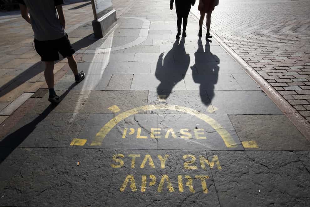 People cast shadows walking past a social distancing information sign painted on the pavement