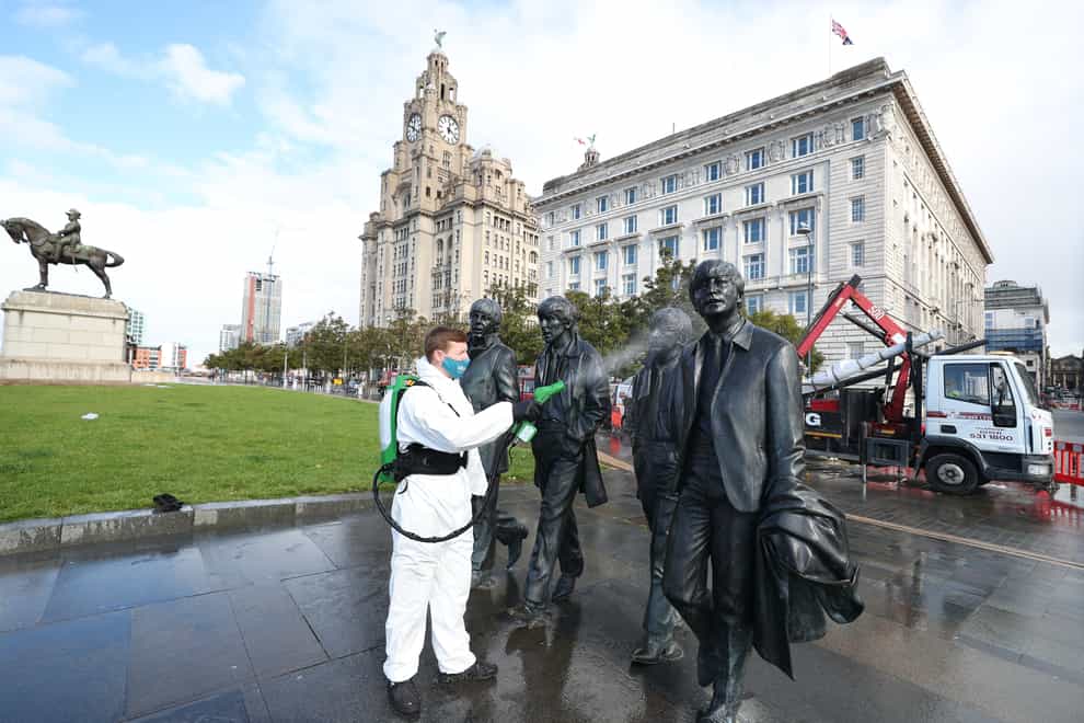 A worker spray cleans the Beatles statue in Liverpool, where tougher Covid-19 restrictions have been announced