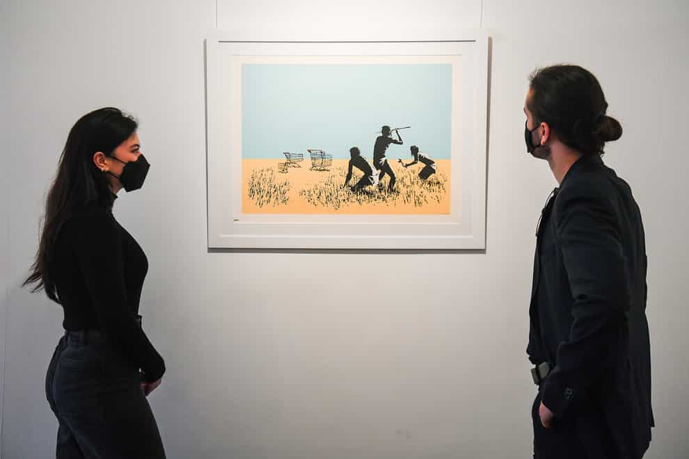 Gallery assistants look at a limited edition print of Trolleys (Colour) (2007) by Banksy, a part of the Catch Me If You Can exhibition