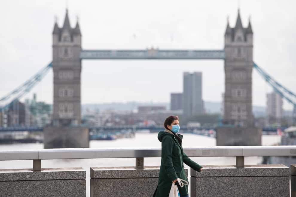 A woman wearing a protective face mask walks over London Bridge in central London, with Tower Bridge in the distance