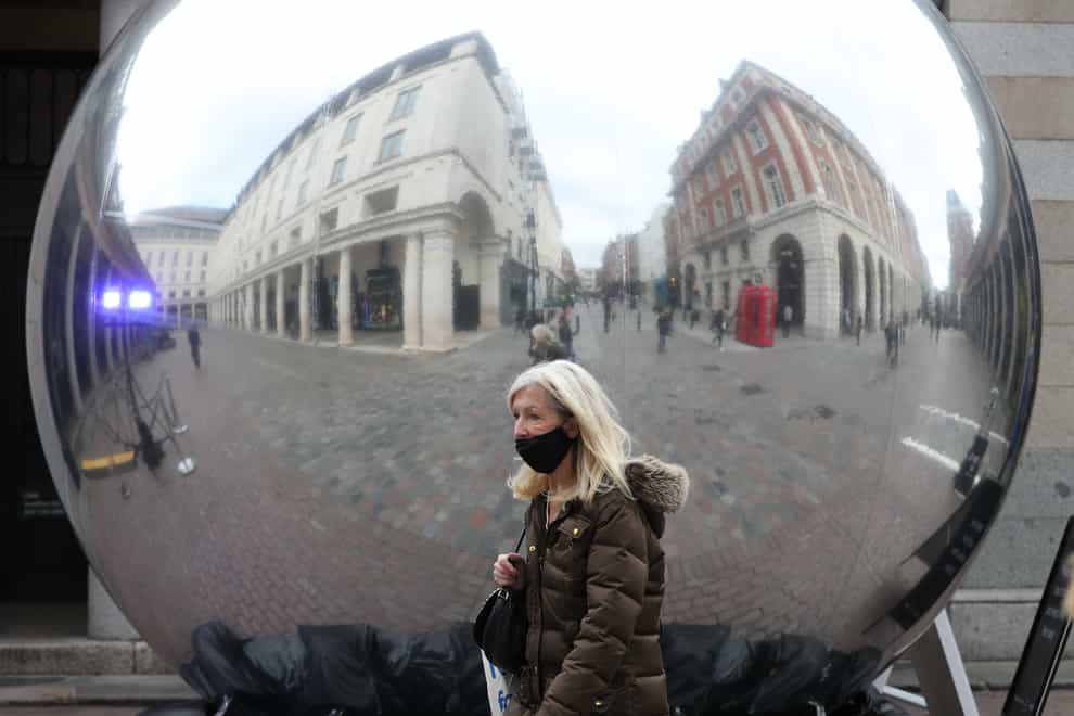 A woman wearing a protective face mask is reflected on the surface of a sculpture in Covent Garden, London