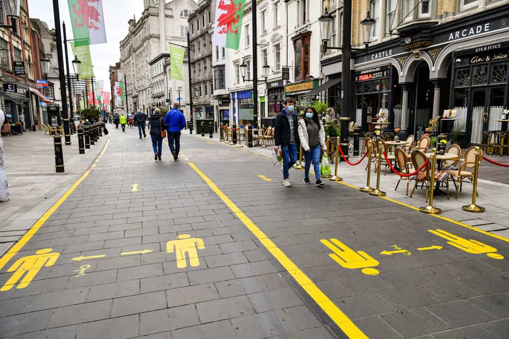 People wear face coverings as they walk along socially distanced floor markings in Cardiff (Ben Birchall/PA)