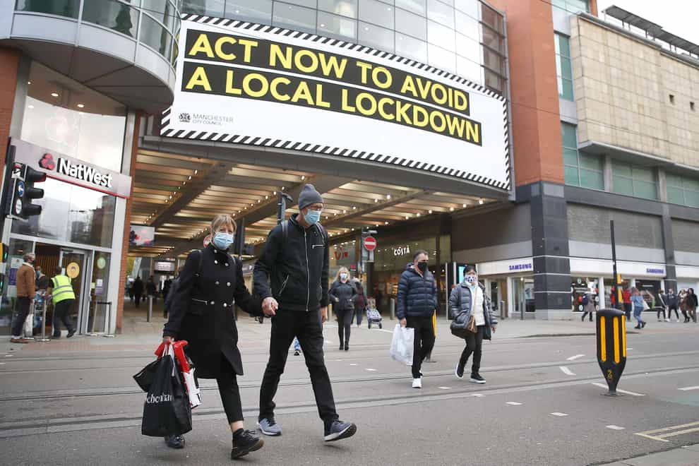 People wearing face masks walk past a advertisement on Market Street in Manchester (Martin Rickett/PA)