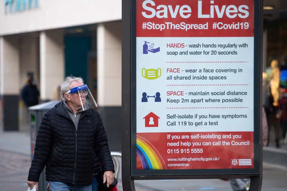 A man wearing a face shield walks past a coronavirus advice sign in Nottingham city centre