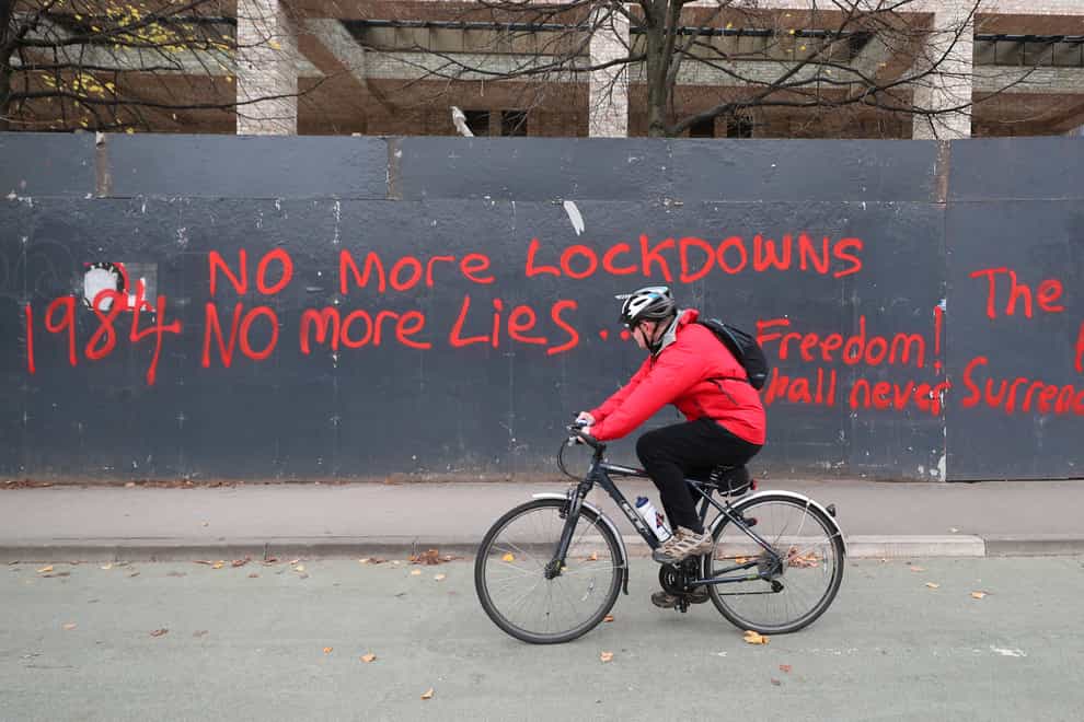 A man cycles past anti-lockdown graffiti in Manchester (Peter Byrne/PA)