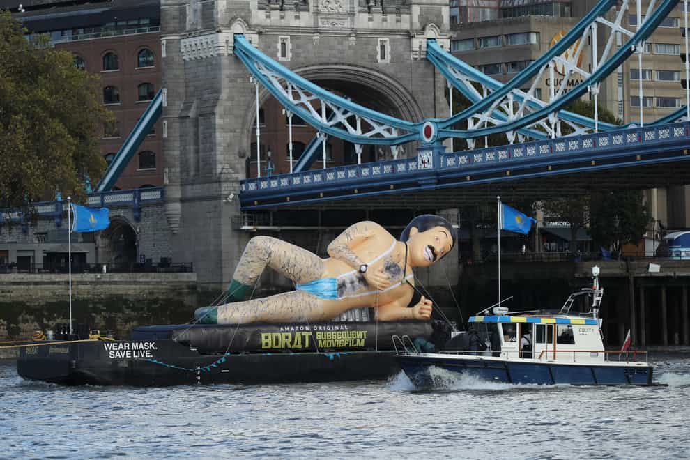 A giant inflatable in the shape of Borat floats on a barge beneath Tower Bridge