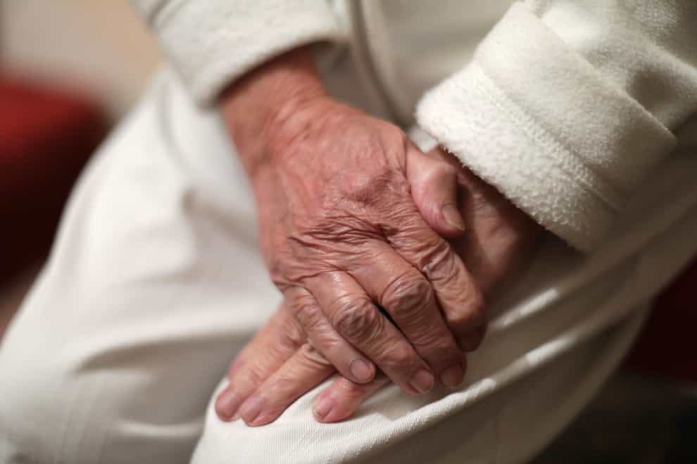 An elderly person with their hands clasped