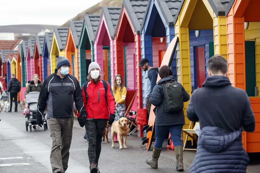 People wear face masks as they walk past beach huts in Saltburn-by-the-Sea.