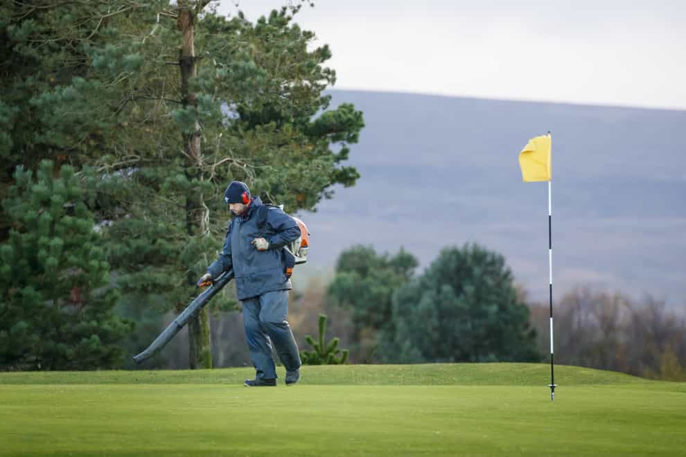 A groundsman blows leaves off a golf course