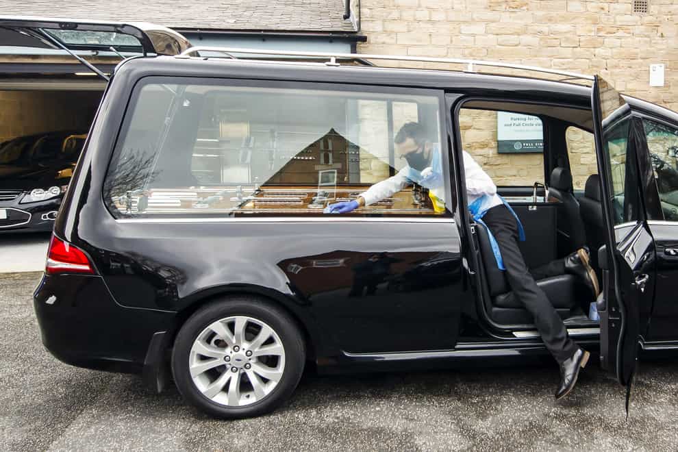Funeral director Andrew Atkins wears PPE as he disinfects a hearse at Full Circle Funerals
