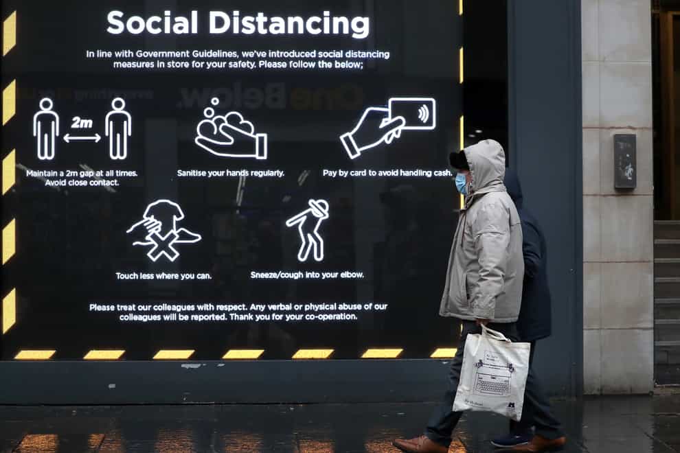 A member of the public walks passed a social distancing sign in a shop window in Glasgow