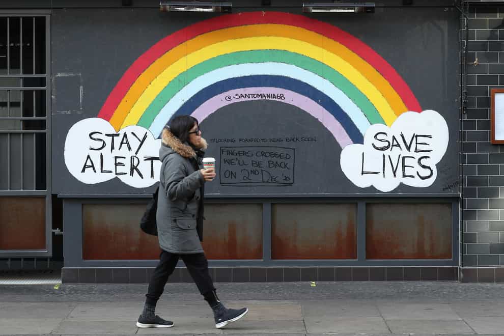 A person walks past a rainbow mural on a closed bar in Soho, London (Yui Mok/PA)