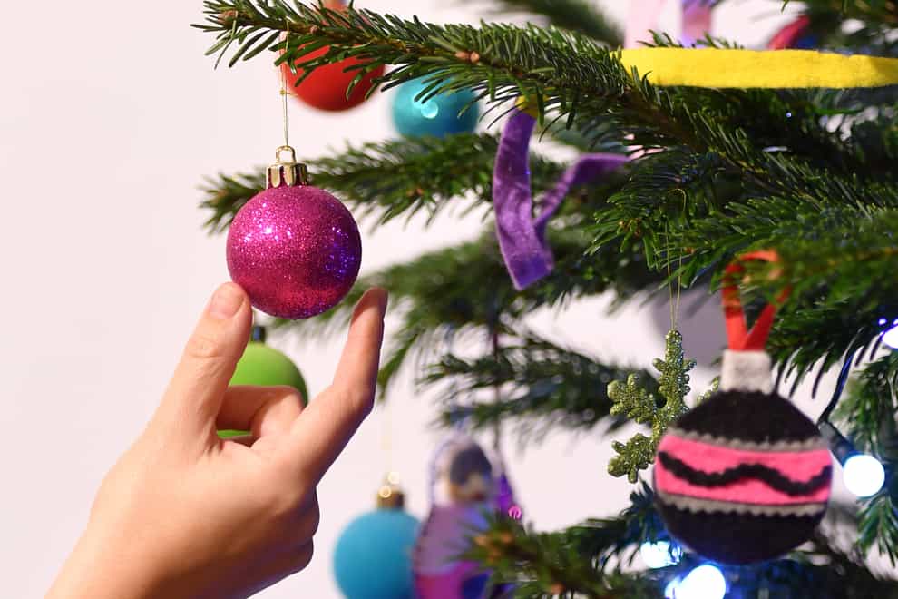 A woman adjusts a decoration on a Christmas tree (Dominic Lipinski/PA)