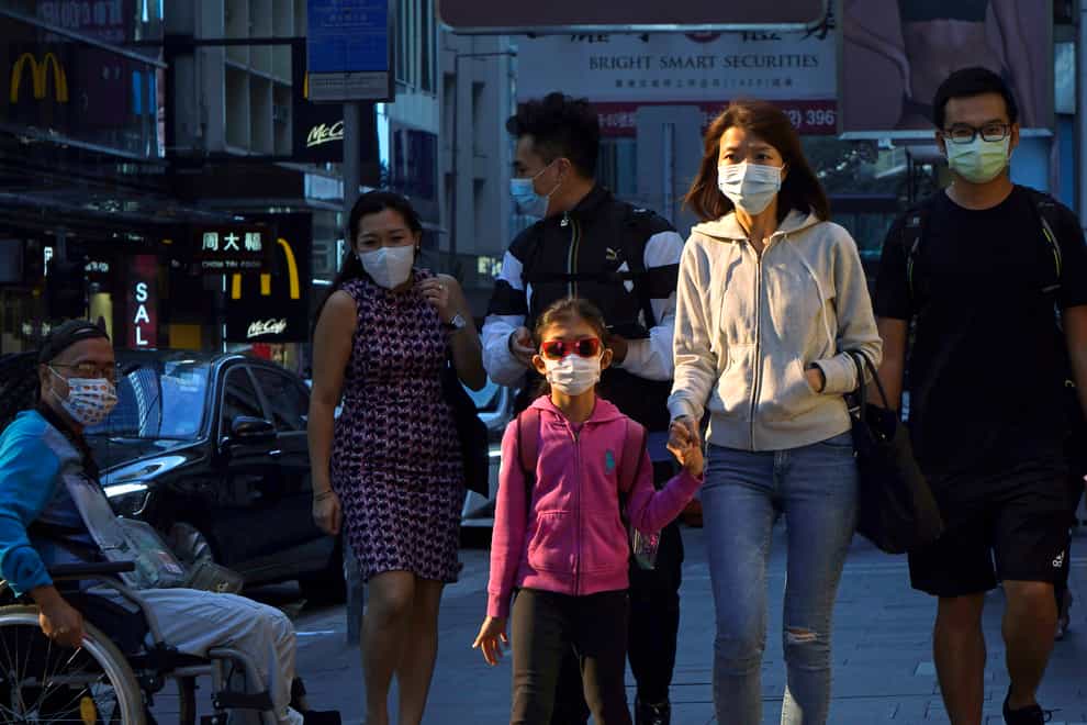 People wearing face masks to protect against coronavirus walk along a street in Hong Kong (KIn Cheung/AP)