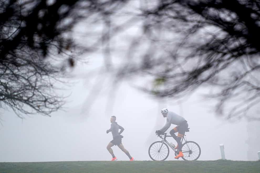 A jogger and a cyclist in the fog in Bushy Park