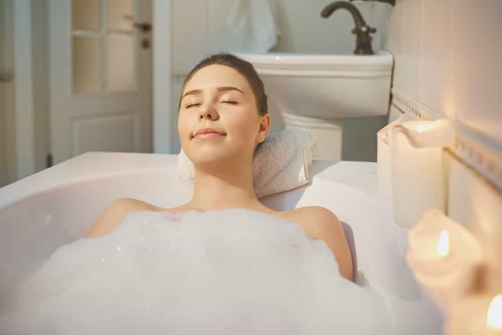 woman is resting in a bathtub with foam in bethroom with candles.