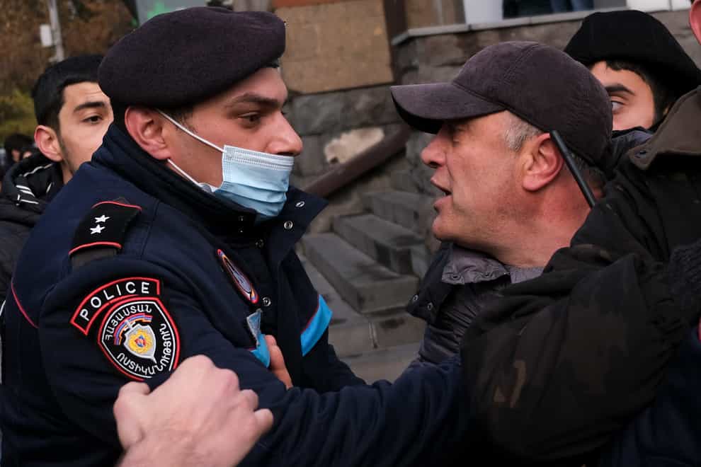 A police officer tries to detain demonstrators during a rally demanding the resignation of Armenia's PM