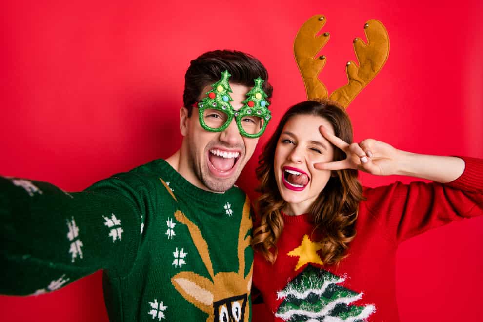 Photo of crazy couple making selfies sticking tongues winking eyes v-signing, wearing Christmas jumpers