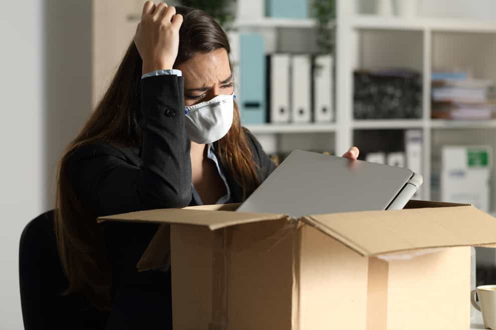 Fired executive woman with protective mask packing personal belongings on a box at the office at night