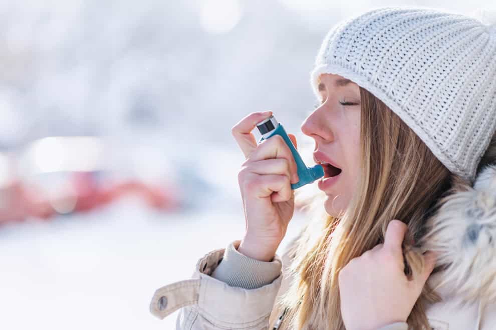 A woman wearing a woolly hat and warm coat using an asthma inhaler