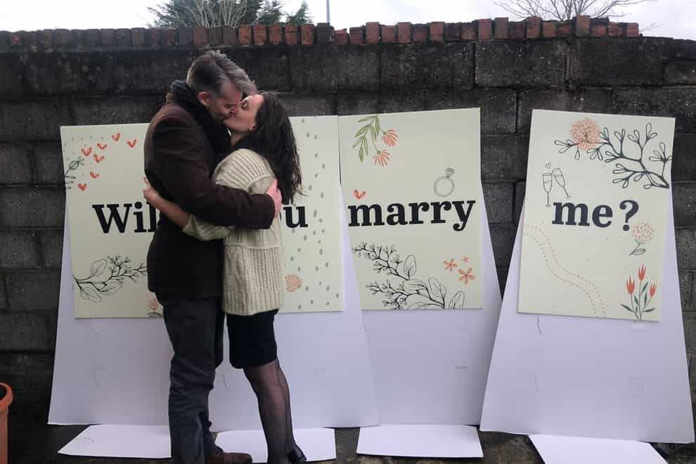 Couple kissing in front of three signs saying 'Will you marry me'