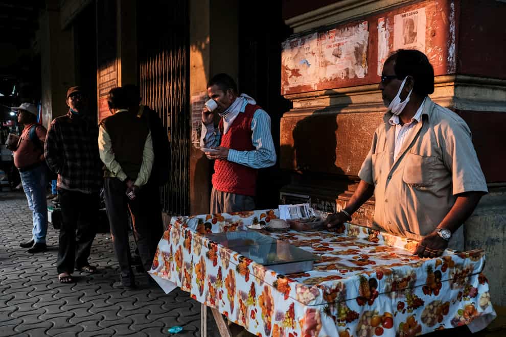 People drink tea as a roadside vendor waits for customers in Kolkata, India
