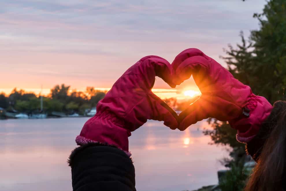 Hands Making Heart Shape around beautiful Sunset wearing Pink gloves – Winter Solstice Love Landscape over water