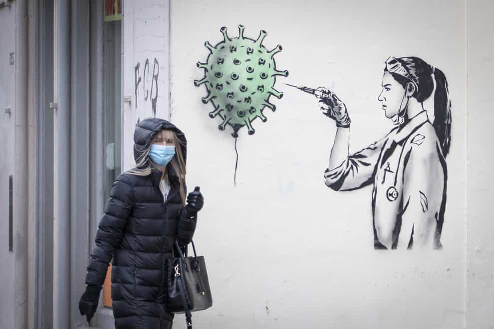 A woman in a mask walks past coronavirus street art in Edinburgh