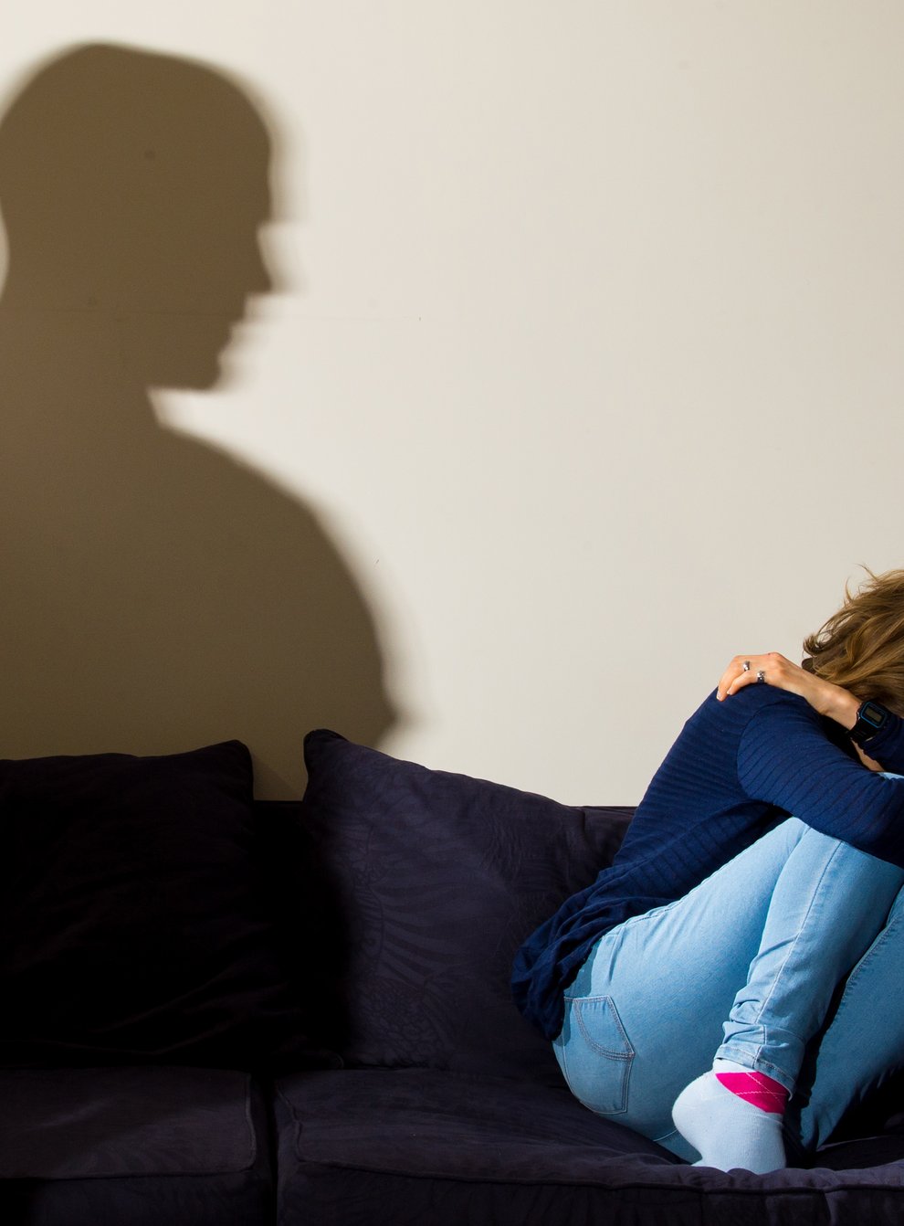 A shadow of a man looming over a woman cowering on a sofa
