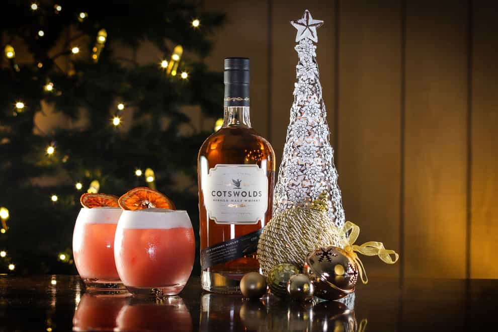 A bottle of Cotswolds Single Malt Whisky and two festive cocktails next to a Christmas tree