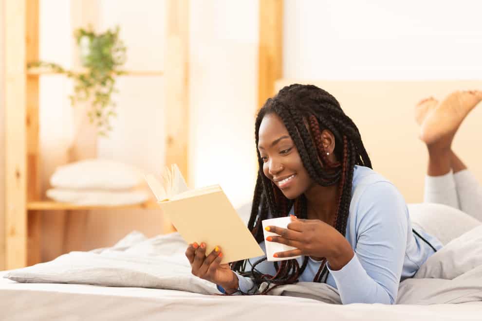 A smiling woman lying on bed reading a book