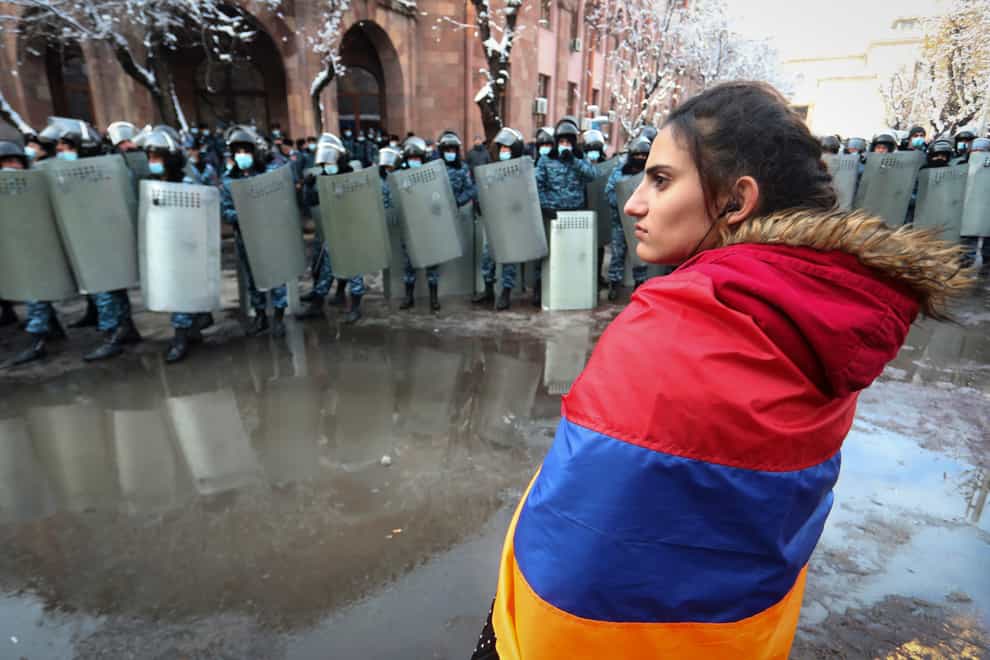 A woman wearing a state Armenian flag stands in front of a riot police line (Vahram Baghdasaryan/AP)