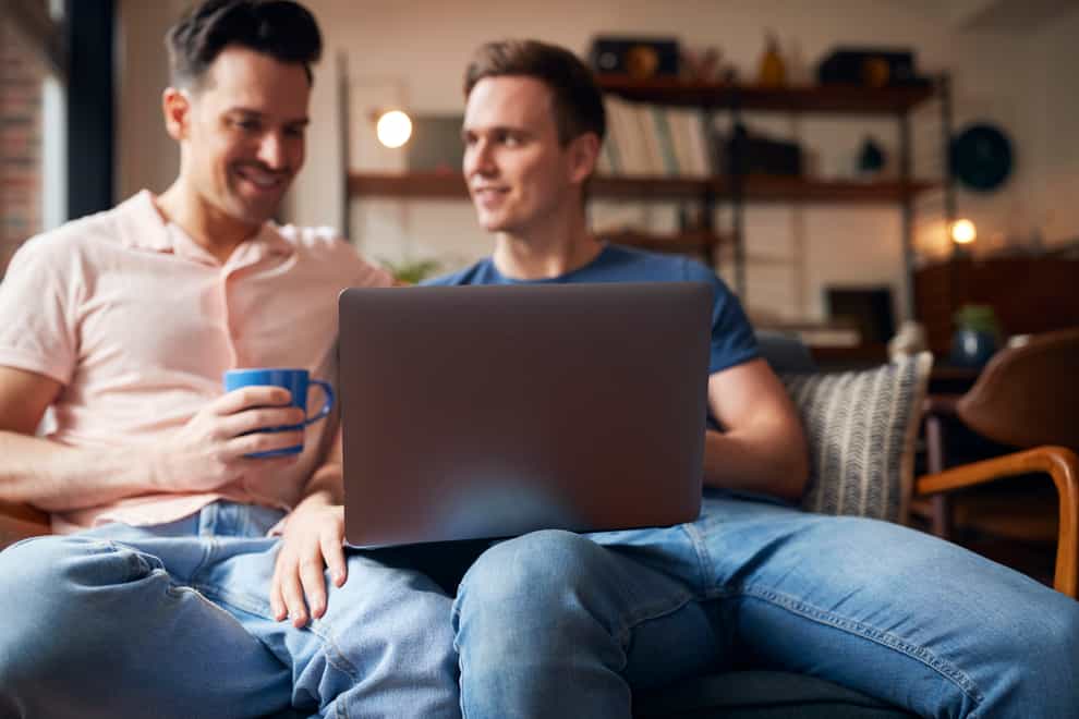 Gay male couple sat together on a sofa looking at properties on a laptop